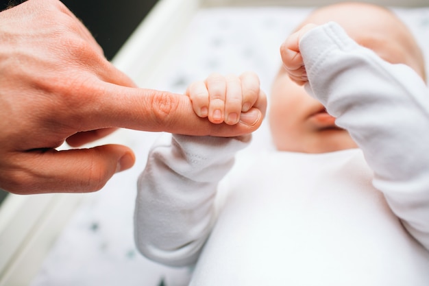 Close-up feet of a newborn baby. Little infant is lying on the kids table . There is Newborn child on the baby changing table near window.