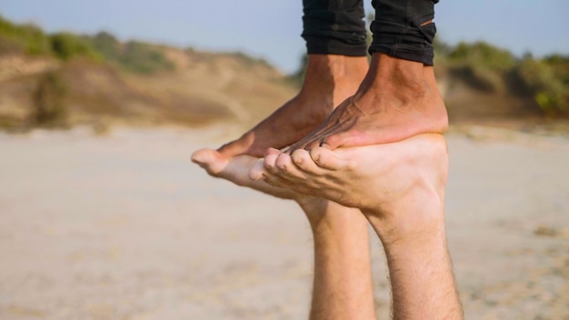 Photo close-up feet of young sporty couple practicing acro yoga with partner together on the sandy beach