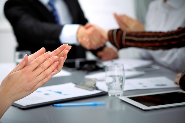 Close up of female applause while business people shaking hands at meeting.