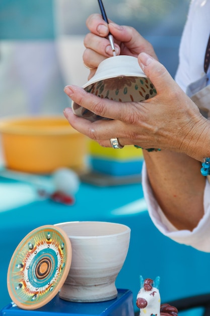 Close-up of the female artist paints clay bowl