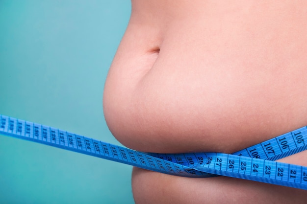 測定テープで包まれた太りすぎのクローズアップ女性の腹、減量のための適切な栄養と食事療法の概念