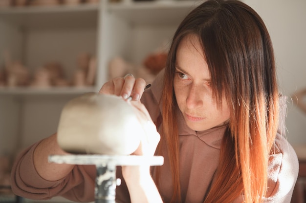 Close up of a female ceramist looking focused while making clay teapot