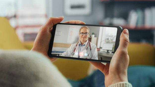 close up of a female chatting in a video call with her female family doctor on smartphone from living room illfeeling woman making a call from home with physician over the internet horisontal vew