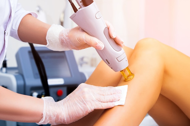 Close-up of a female cosmetologist in a medical coat making a young woman  a procedure laser hair removal for leg. Cosmetology, ionization, diamond procedures.