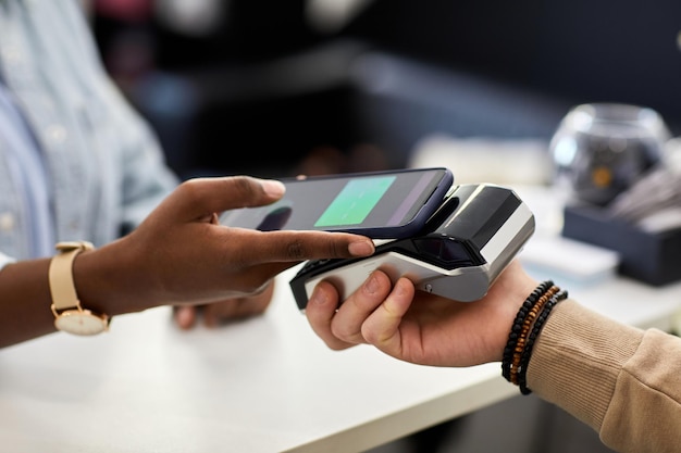 Close up of female customer paying in clothing store via smartphone nfc copy space