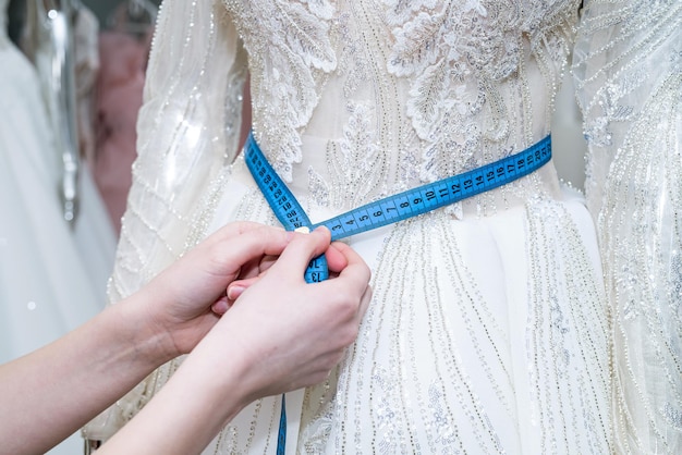 Primo piano di una sarta di design femminile che si adatta a mano abito da sposa con nastro di misura in boutique