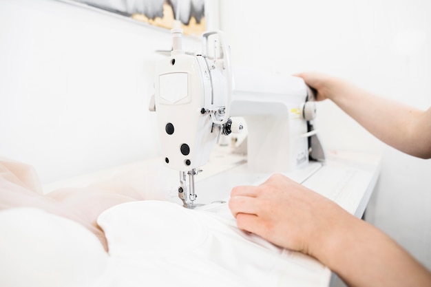 Foto primo piano della mano di un designer femminile che lavora alla macchina da cucire