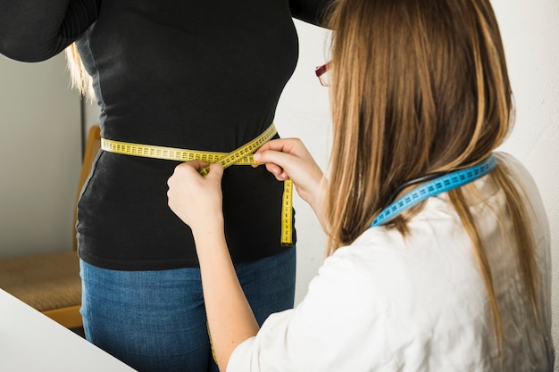 Photo close-up of a female dietician measuring patient belly in clinic