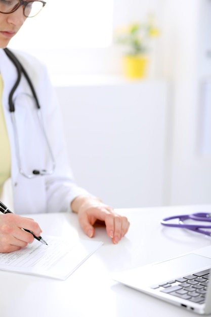 Close-up of a female doctor filling out application form , sitting at the table in the hospital