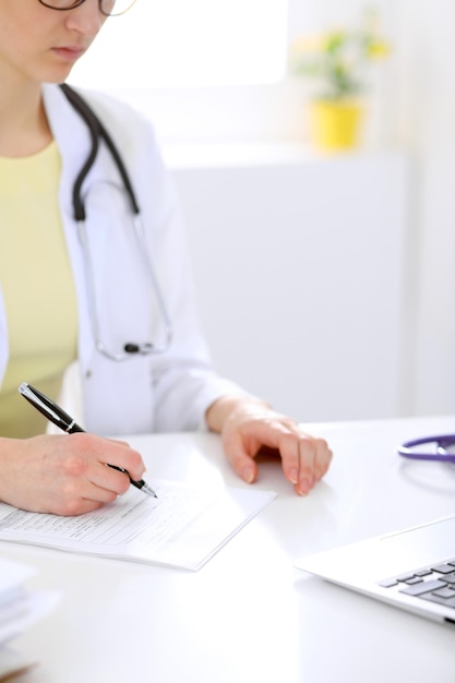 Close-up of a female doctor filling  out application form , sitting at the table in the hospital