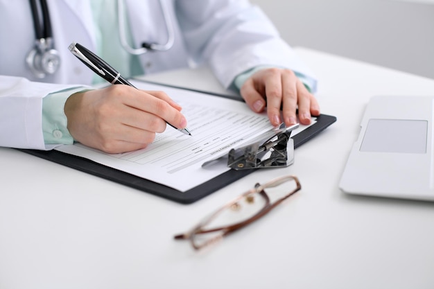 Close-up of a female doctor filling  out application form , sitting at the table in the hospital