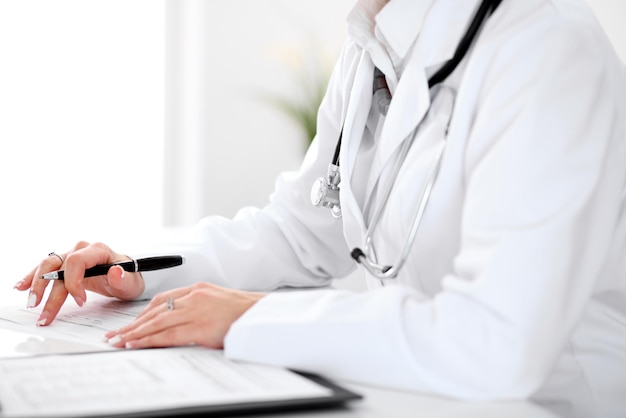 Close-up of a female doctor filling  out application form , sitting at the table in the hospital