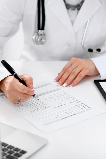 Close-up of a female doctor filling  out application form , sitting at the table in the hospital