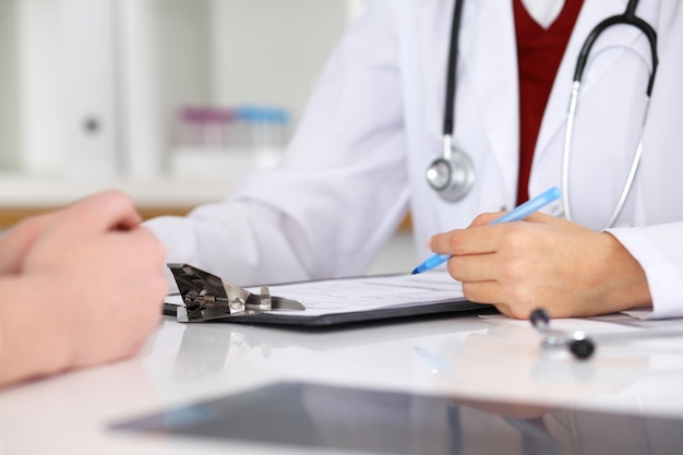 Close up of a female doctor filling up  an application form while consulting patient. Medicine and health care concept