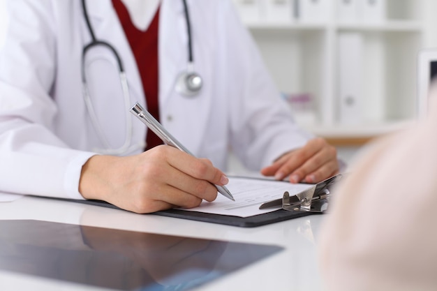 Close up of a female doctor filling up  an application form while consulting patient. Medicine and health care concept