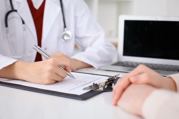 Close up of a female doctor filling up  an application form while consulting patient. Medicine and health care concept