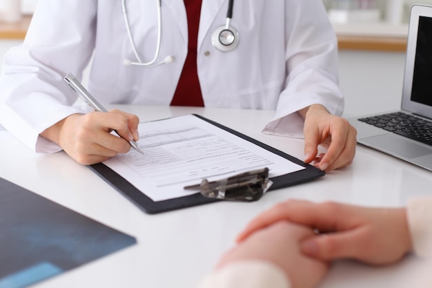 Close up of a female doctor filling up  an application form while consulting patient. Medicine and health care concept