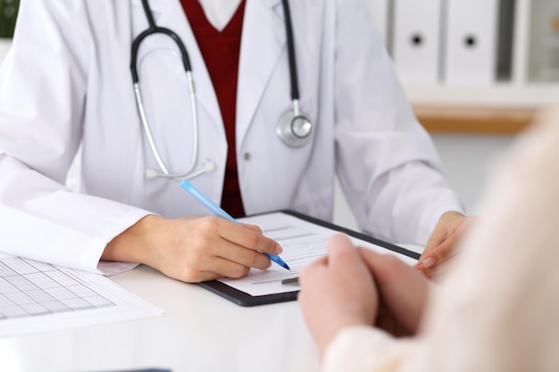 Close up of a female doctor filling up an application form while consulting patient