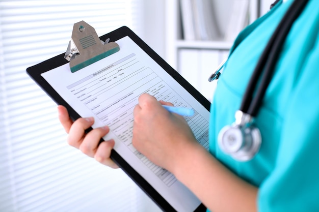 Close-up of a female doctor is filling  out application form or medical history