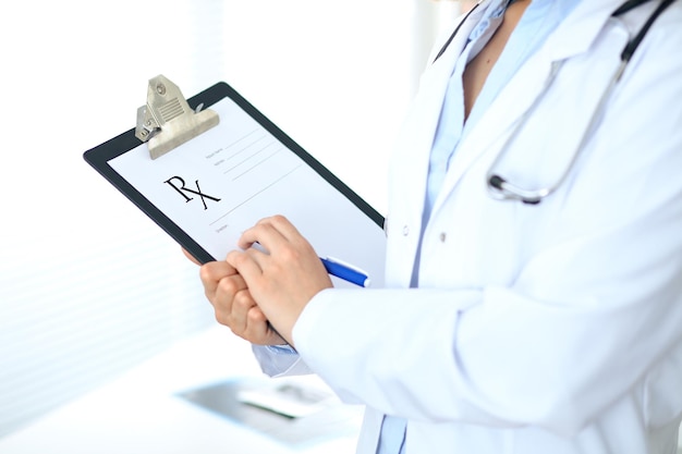 Close up of  female doctor  writing a medical prescription at clipboard while standing