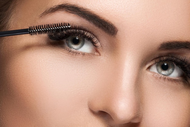 Close-up of female face and mascara wand for maximum volume of artificial eyelashes