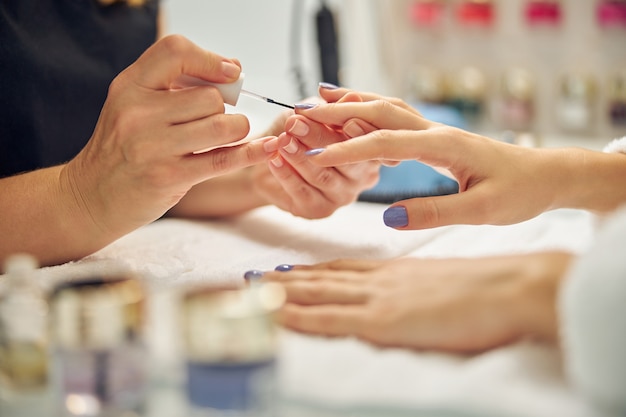 Close up of female fingers during manicure procedure with colour gel polish by nail artist