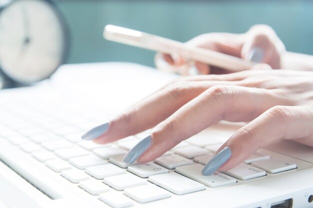 Close up of female fingers using laptop and mobile device, working woman and online shopping concept