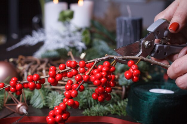 モミの枝、クリスマスの泡、自然の装飾のクリスマスリースを作る女性の花屋のクローズアップ