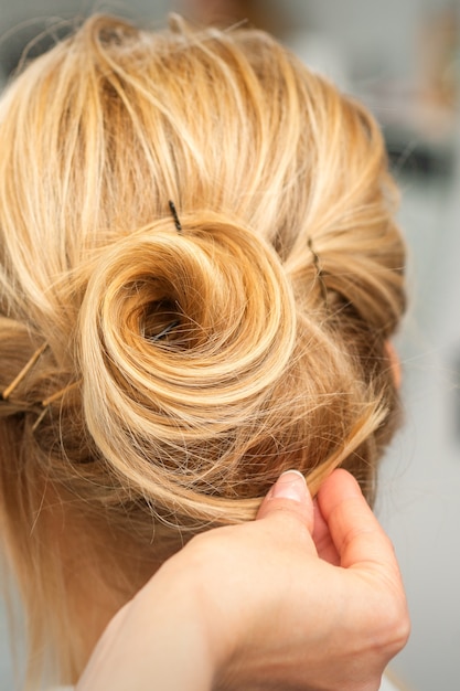 Chiuda in su del parrucchiere femminile per lo styling dei capelli biondi di una giovane donna in un salone di bellezza