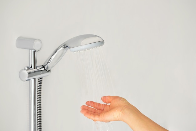 Photo close-up of a female hand checks the temperature of the water in the shower with a hand-held wall-mounted shower.