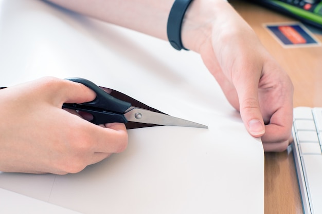 Close-up female hand cuts white paper with scissors. Creativity concept, handmade, holiday.