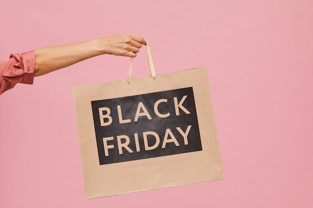 Close-up of female hand holding Black Friday shopping bag against the pink background