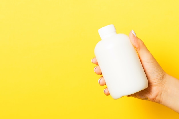 Close up of female hand holding cosmetics bottle at yellow background with copy space.