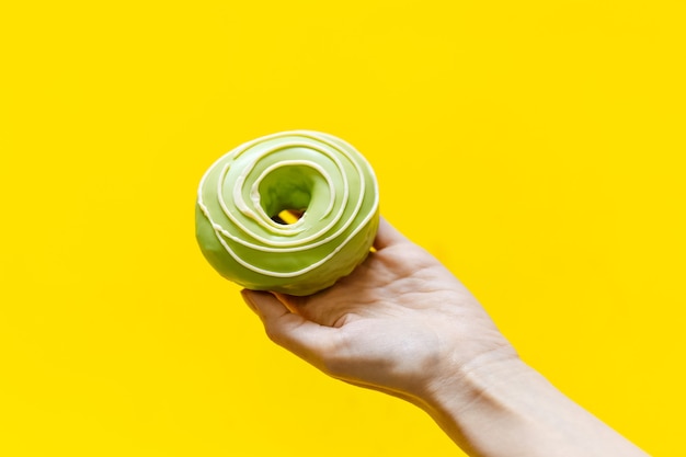 Close-up of female hand, holding green donut on yellow