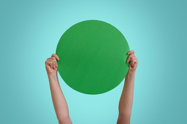 Photo close up of  female hand holding green paper round, isolated over blue studio background wall with c