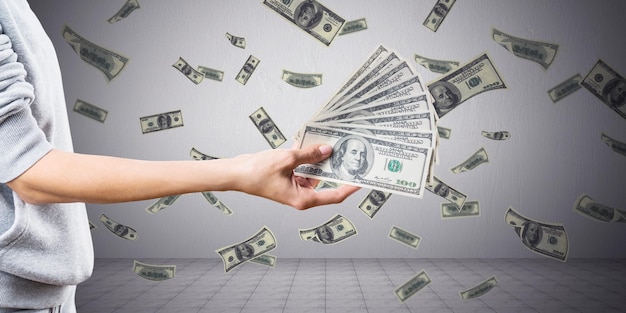 Крупный план женской руки, держащей деньги с творческим дождем долларовых банкнот на фоне бетонной стены Миллионер богат и наличными концепция
