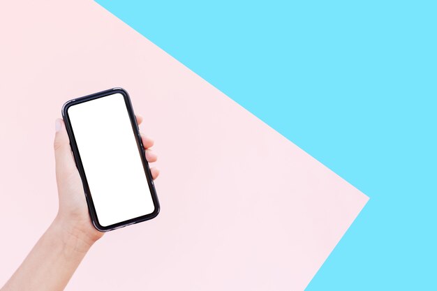 Primo piano della mano femminile che tiene smartphone con mockup su superfici di rosa pastello e blu di colori