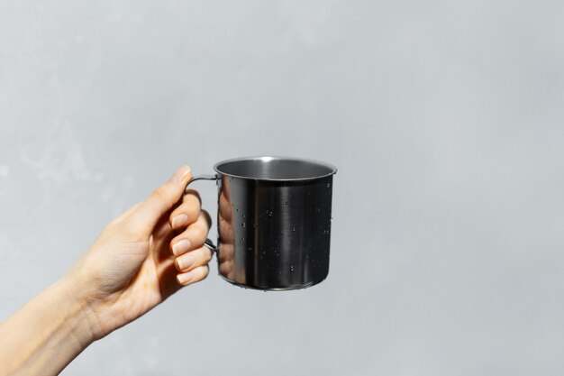 Close-up of female hand holding steel mug on  grey wall