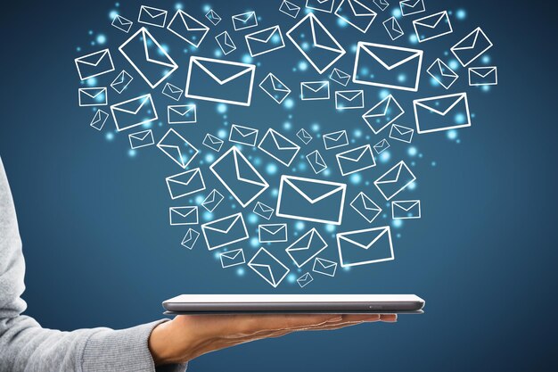 close up of female hand holding tablet with creative drawn email icons on blue background business technology communication and email marketing concept