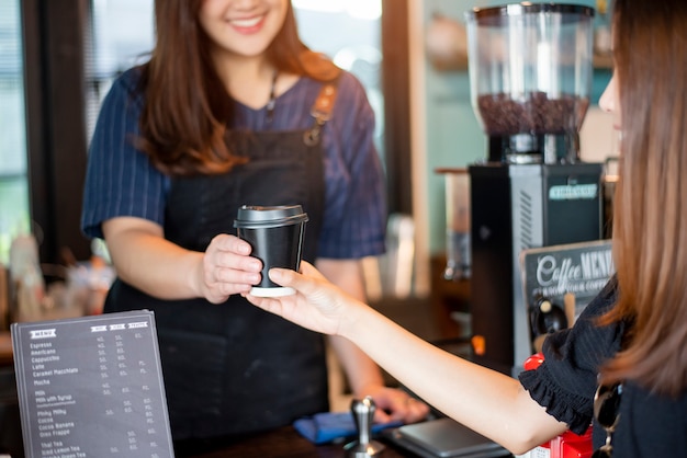 女性の手のクローズアップは、バリスタからホットコーヒーを取っています。