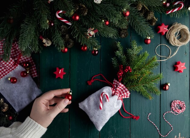 Close-up female hand prepares a pouch with a gift on a green wooden table in a Christmas decor