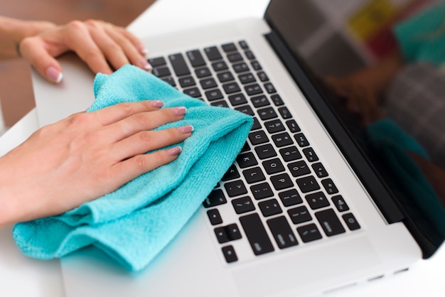 Primo piano della mano femminile che pulisce la tastiera del computer portatile con tessuto blu