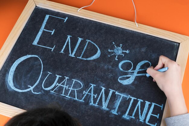 Photo close up of female hand writing the lettering end of quarantine on chalkboard with blue chalk