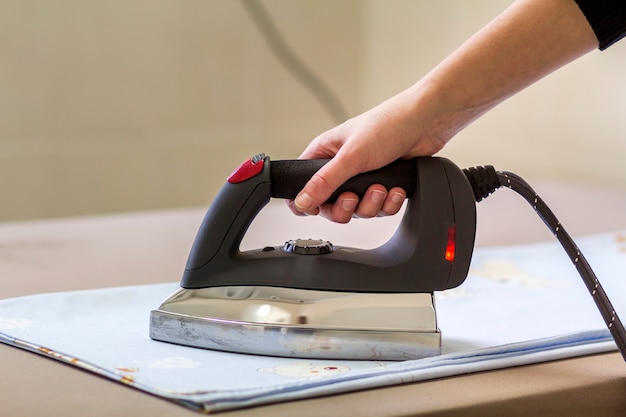 Close-up of female handle ironing clothing using new modern stainless steel iron with teflon sole and steam generator isolated on light copy space background.