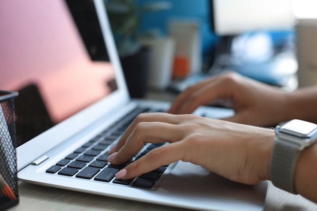 Крупным планом женские руки заняты набором текста на ноутбуке в современном офисе.
