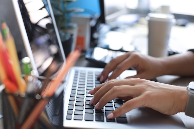 Foto primo piano di mani femminili impegnate a digitare sul computer portatile in un ufficio moderno.