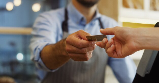 Primo piano delle mani femminili dell'acquirente dando una carta di credito per il pagamento al venditore maschio nel negozio di panetteria. interno