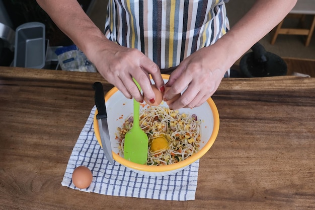 卵を割って野菜のパテを作る女性の手のクローズ アップ