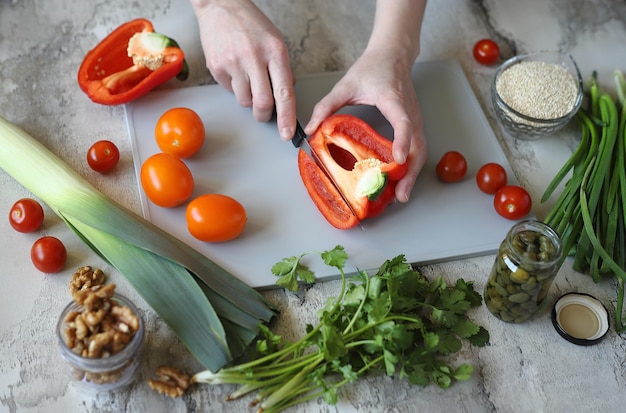 鋭いナイフでまな板の上のトマトを切る女性の手のクローズ アップ 健康食品のコンセプトを調理