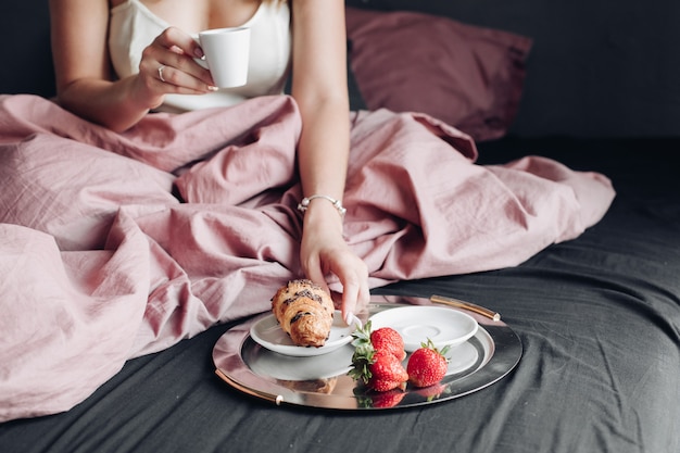 Close-up female hands enjoying weekend having appetizing breakfast in bed